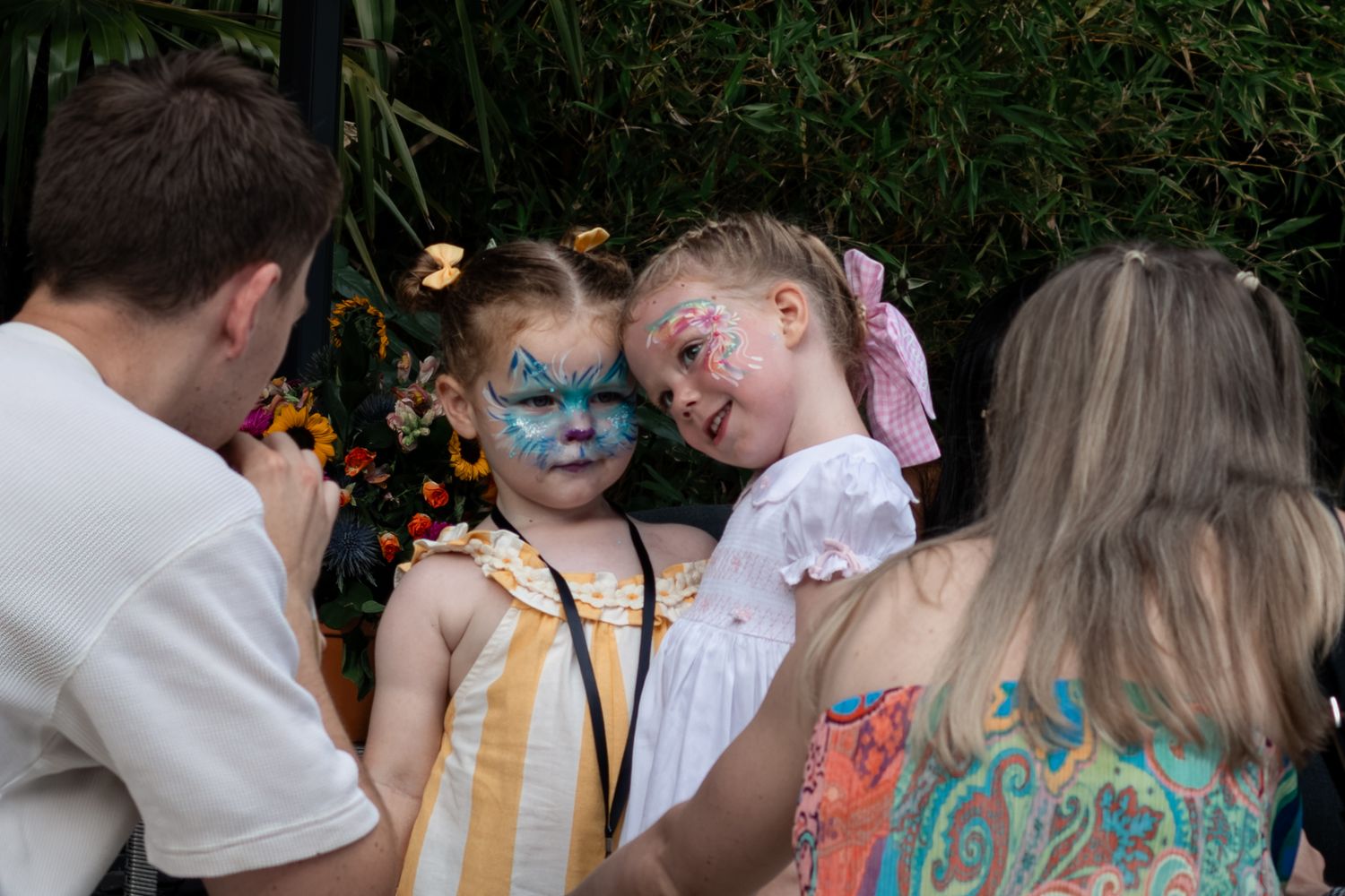 Two young girls with butterfly face paint smiling at outdoor garden party event.