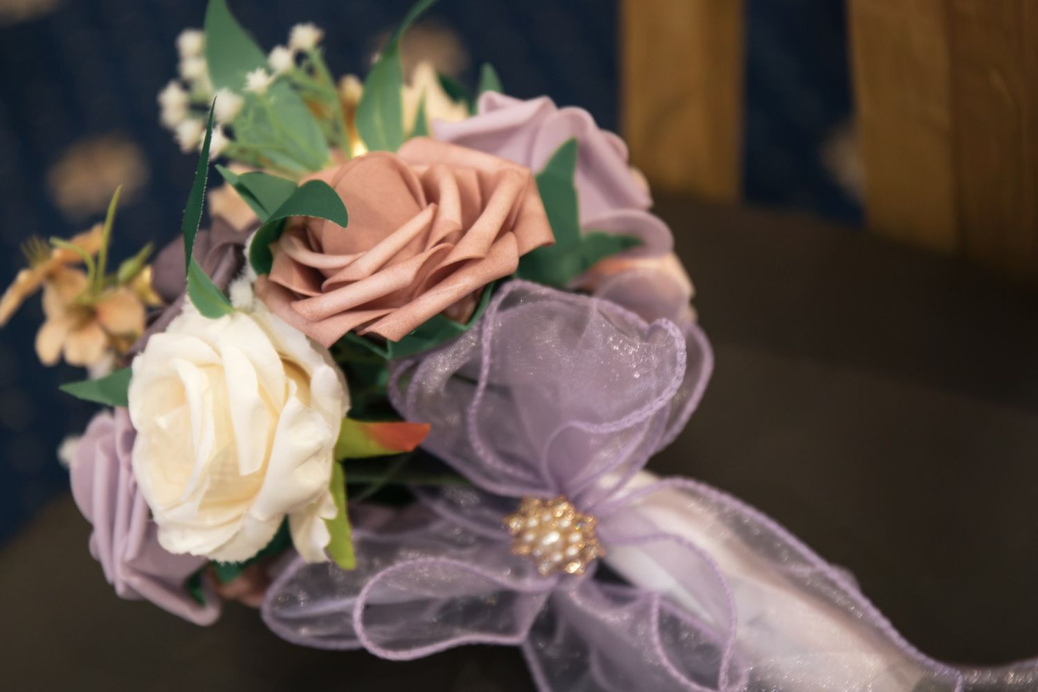 Elegant bridal corsage with mauve roses, cream flowers, and purple tulle ribbon.