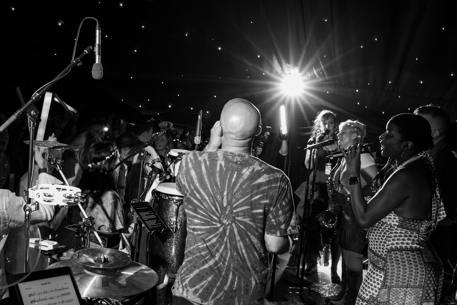 Black and white photo of a large band performing on stage under bright lights at a nighttime music event.