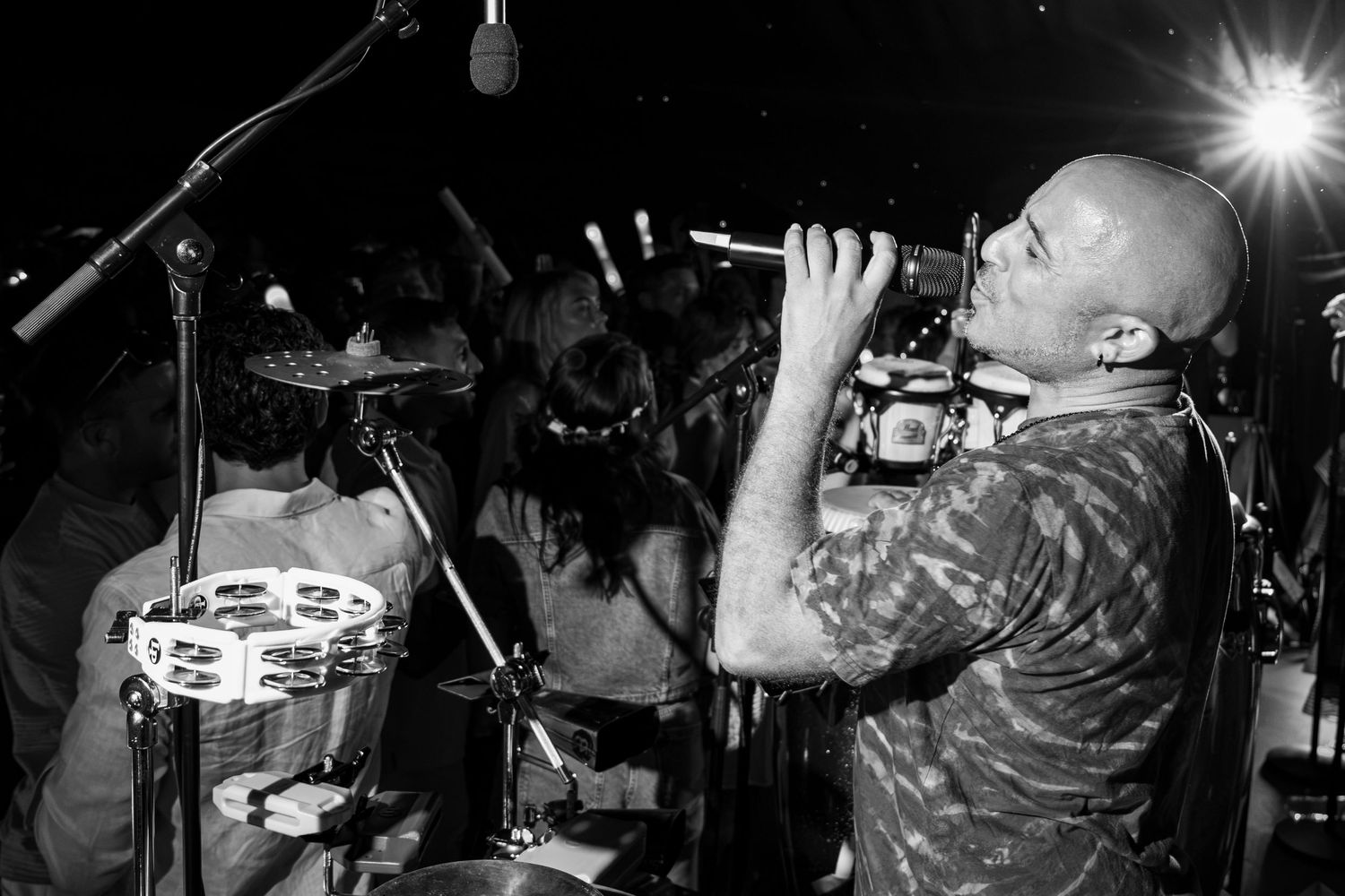 Black and white photo of a bald musician playing a wind instrument on stage at a live music performance.