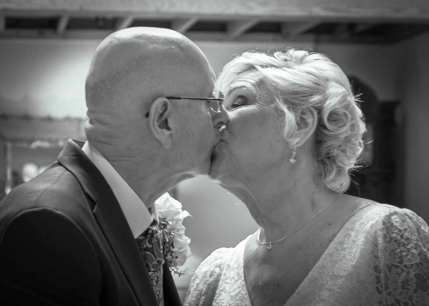 Elderly couple sharing a romantic kiss at their wedding ceremony in a black and white photo.