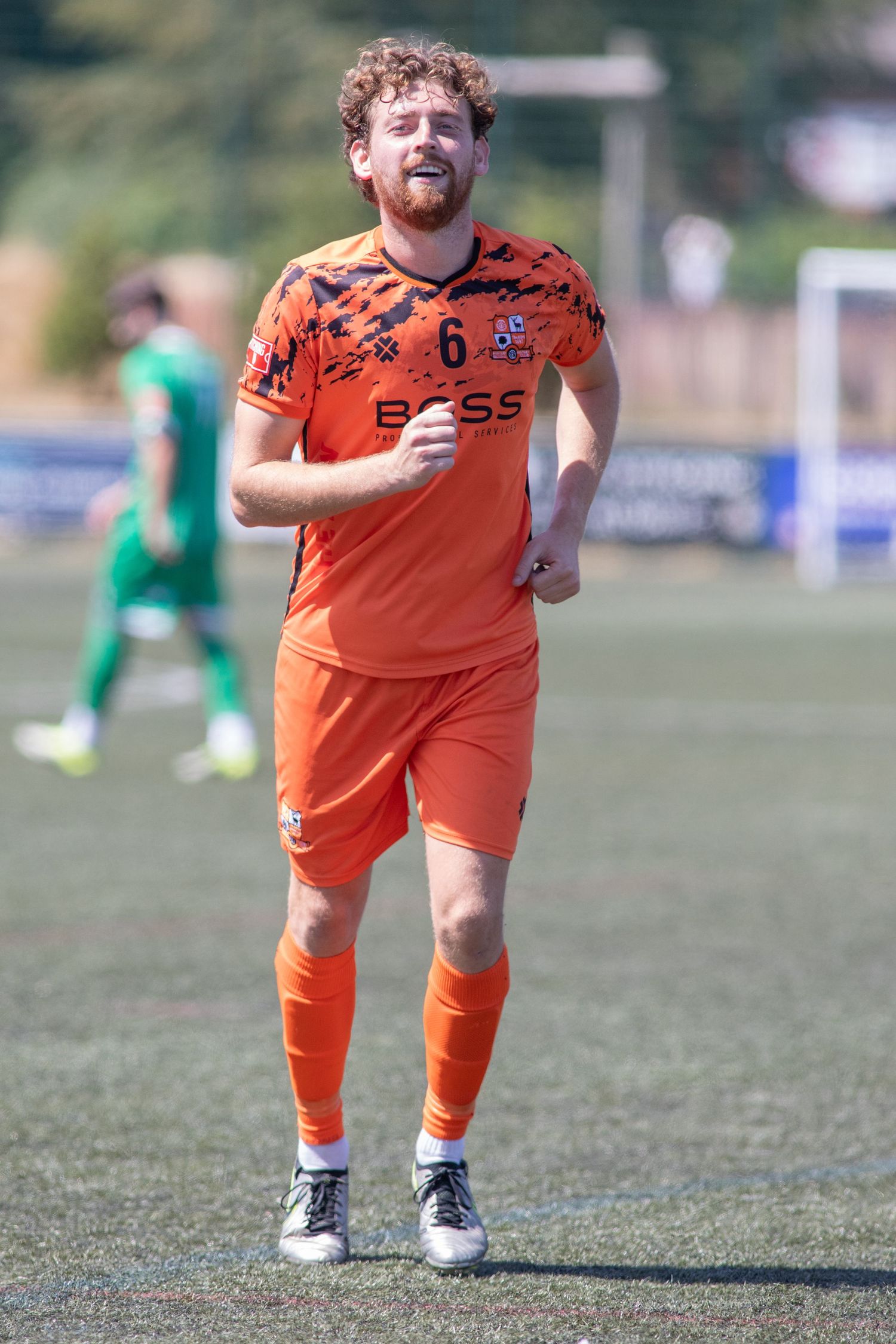 Male soccer player in orange BOSS kit running during a sunny outdoor football match.