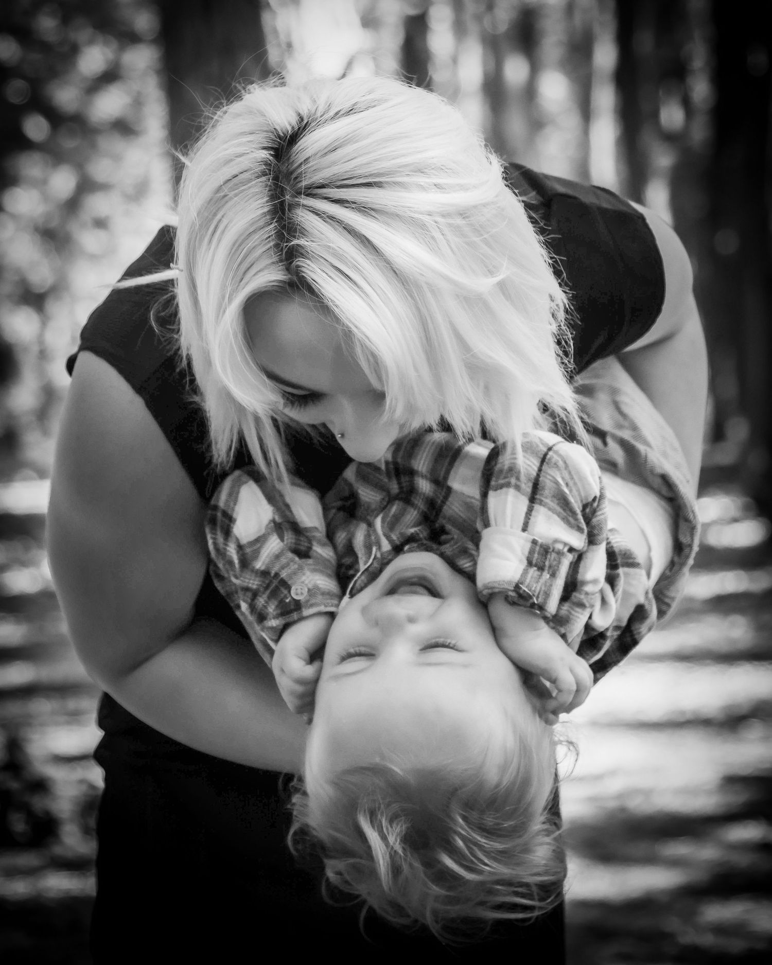 Black and white photo of a mother playfully dipping her laughing toddler son outdoors.