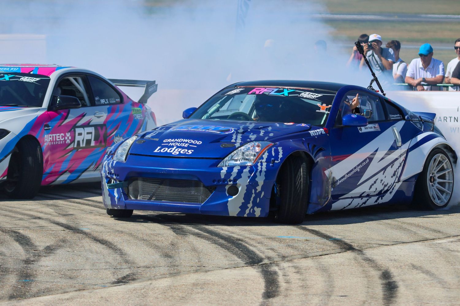 Blue Lodges sponsored Nissan 350Z drift car creating tire smoke on a competition circuit.