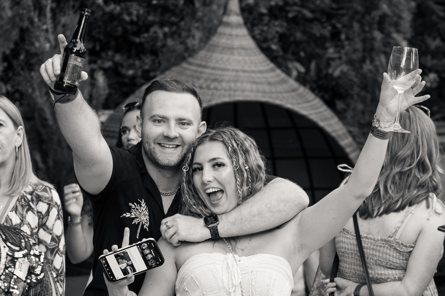 Man and woman celebrating outdoors raising drinks at a festive wedding party event.