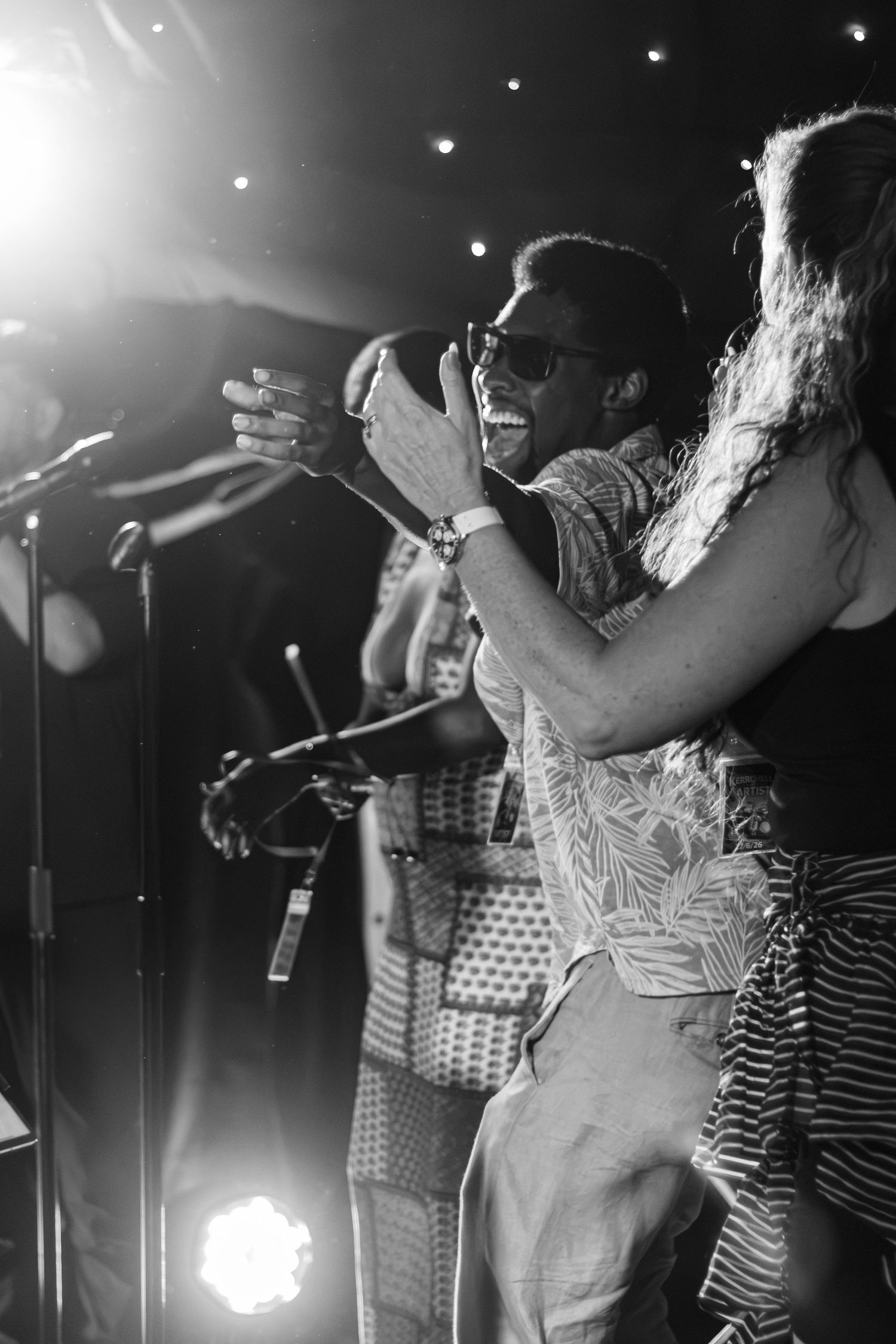 A smiling performer on stage clapping hands in black and white photo.