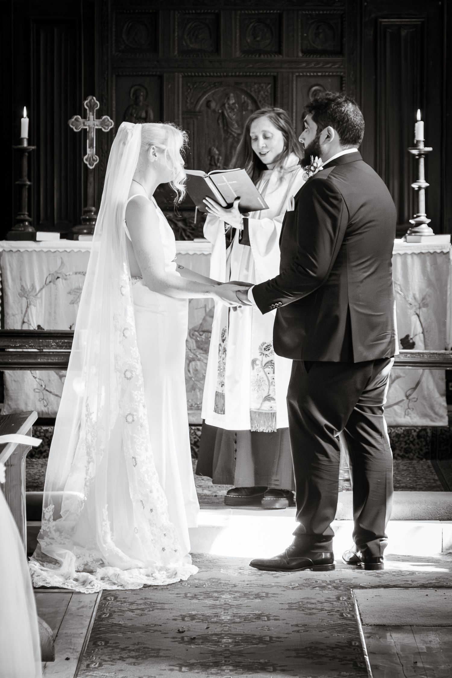 Black and white photo of bride and groom exchanging vows at church altar.