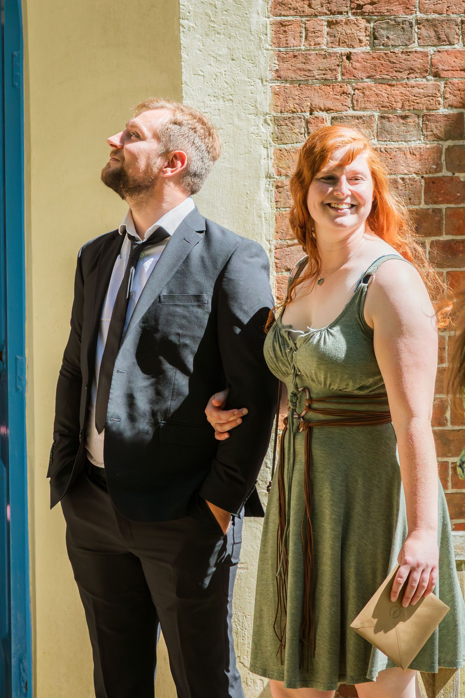 Smiling redhead woman in green dress standing with bearded man in suit outdoors.