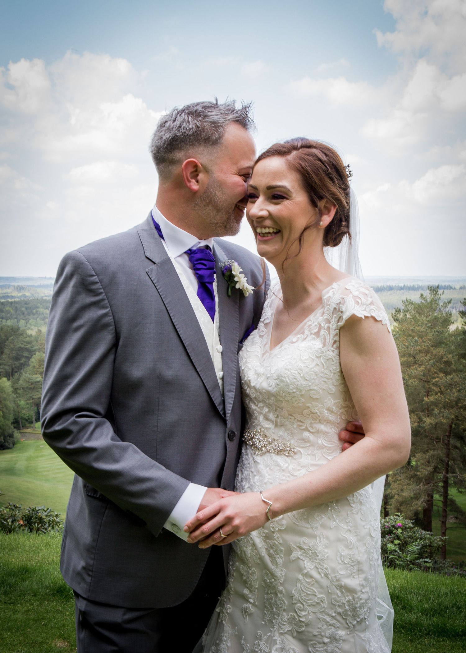 Happy bride and groom sharing romantic moment with scenic countryside backdrop on wedding day.