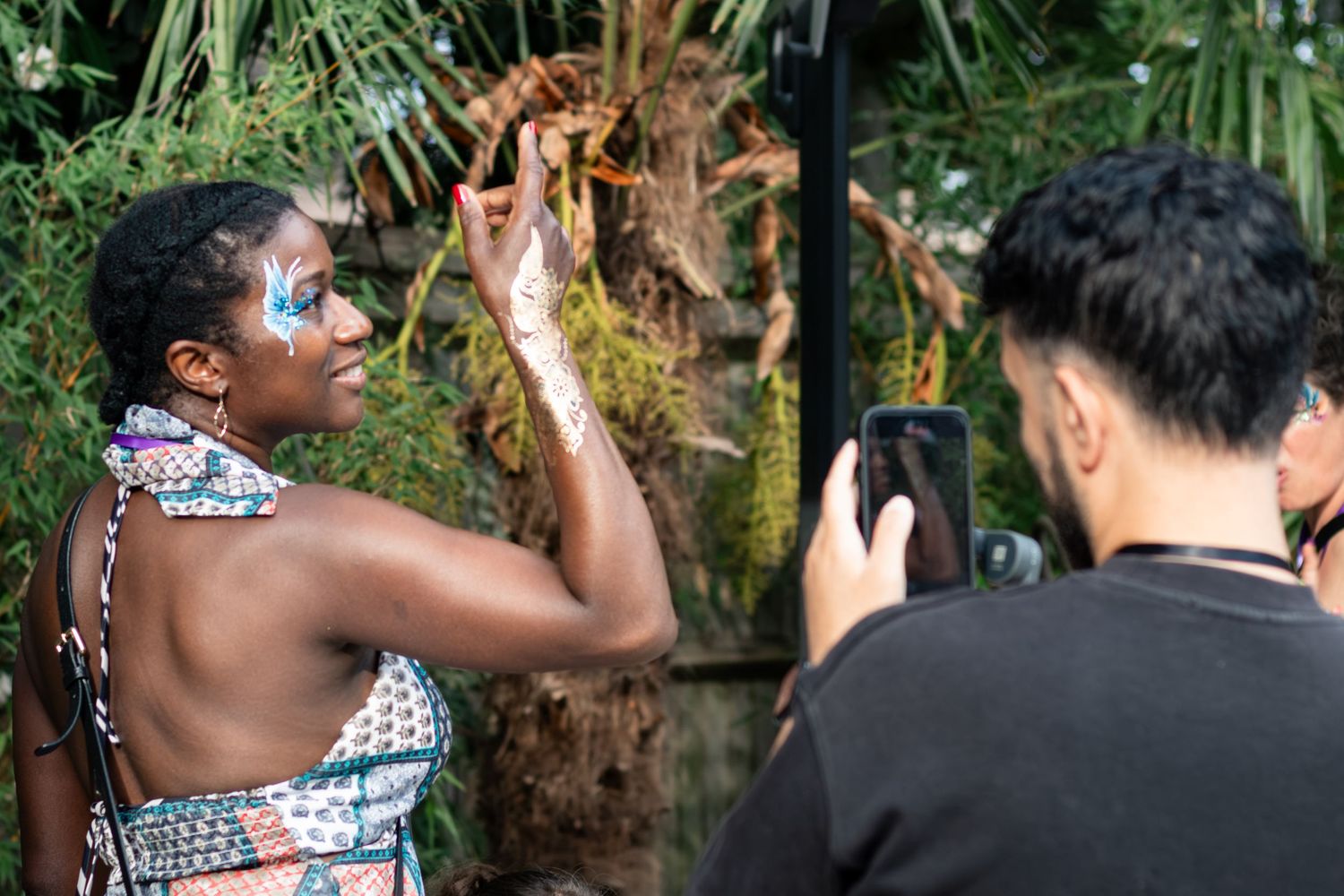 A woman with decorative face paint poses while a man photographs her at an outdoor cultural festival event.