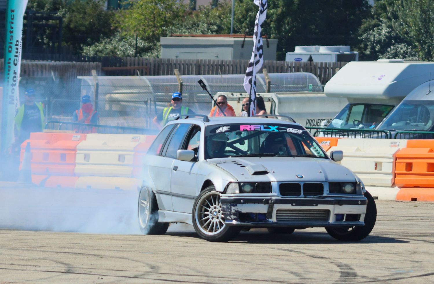 Silver BMW E36 estate wagon drift car performing a smoky burnout at an RFLX drift event.