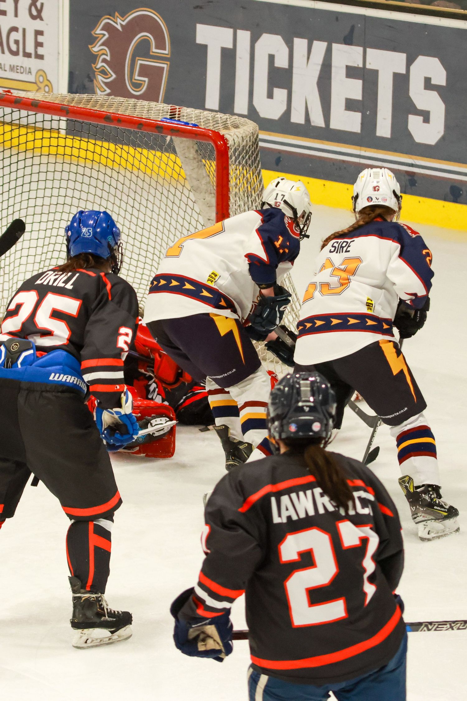 Ice hockey players battle in front of red goal net with players Drill number 25 and Lawrence number 27 in black uniforms.