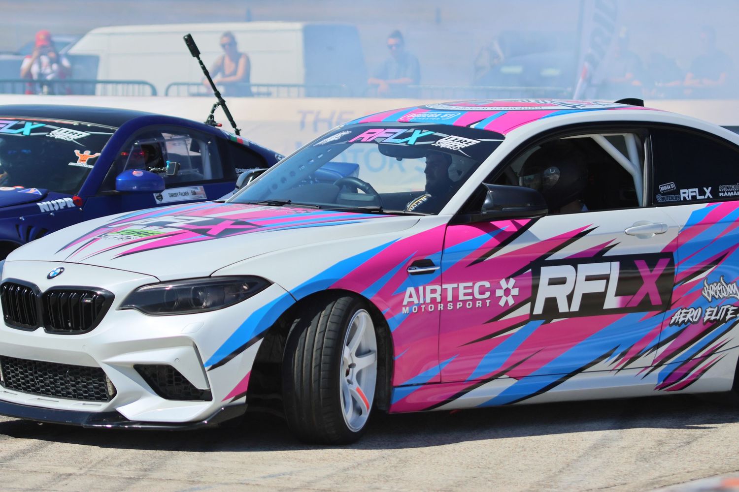 Pink and blue RFLX Airtec Motorsport BMW M2 drift car competing on a race circuit.