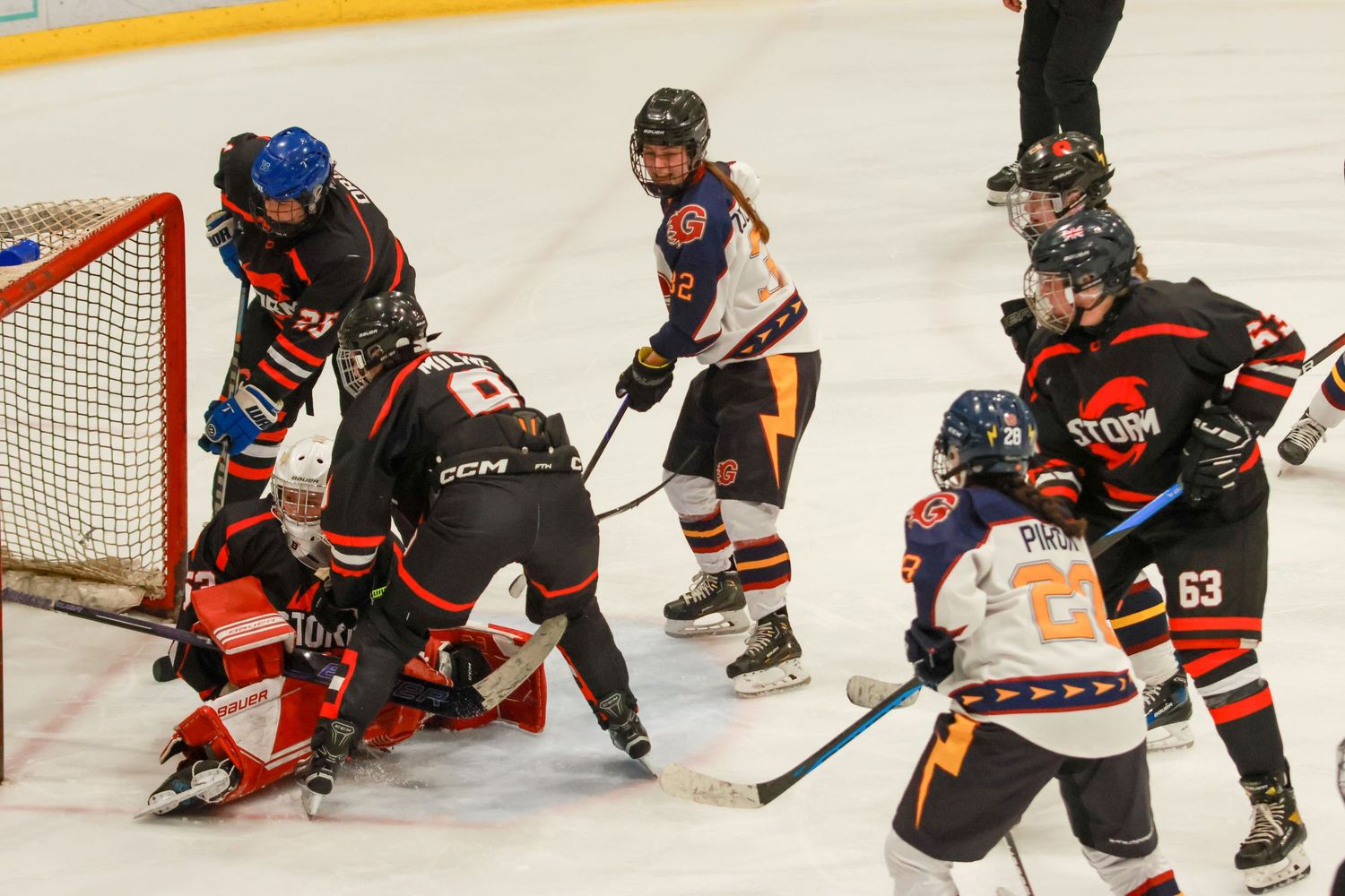 Youth ice hockey players crowd the goal crease during a competitive Storm team hockey game.
