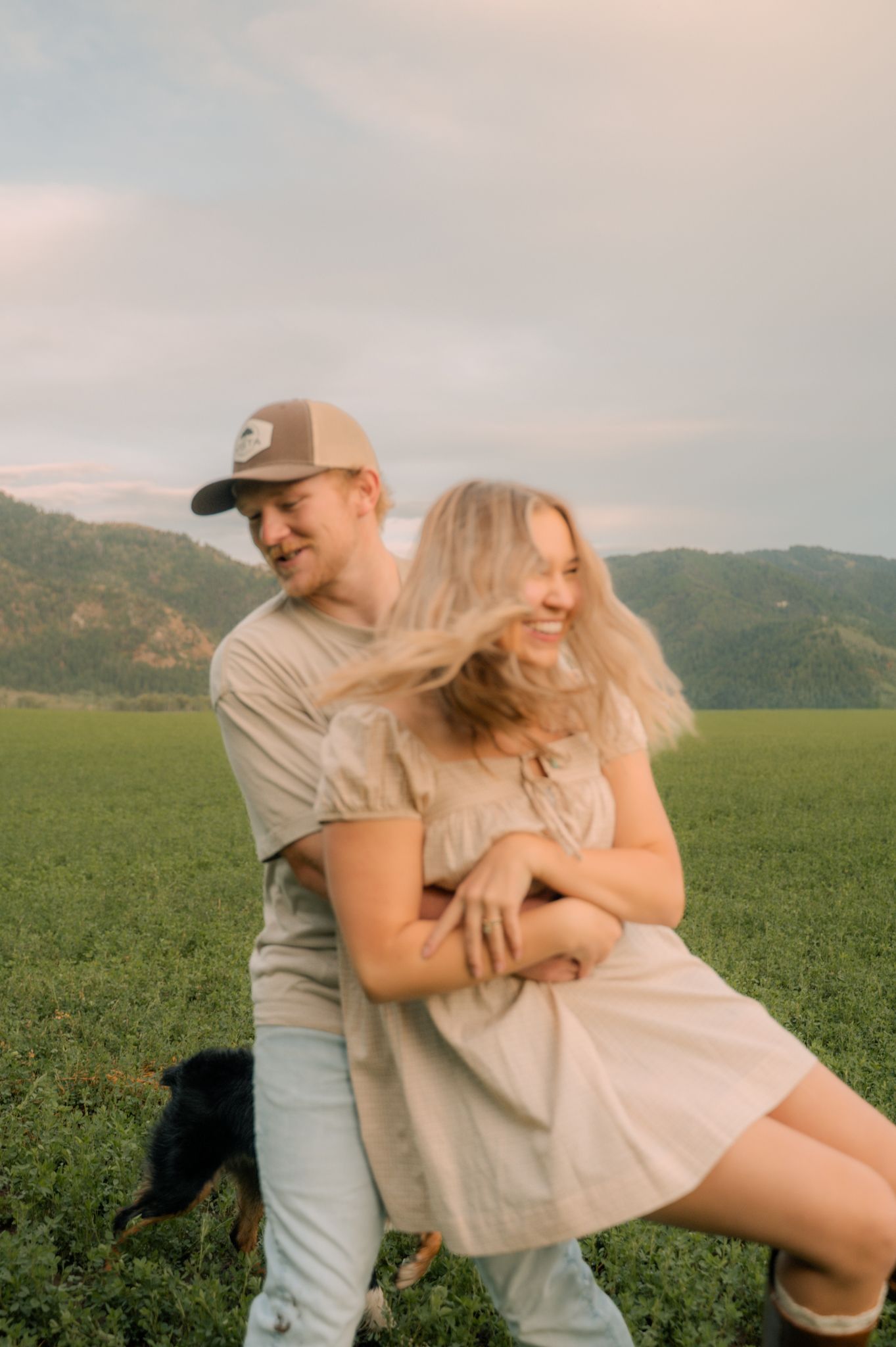 Young couple laughing and dancing together in a green field with mountain backdrop.