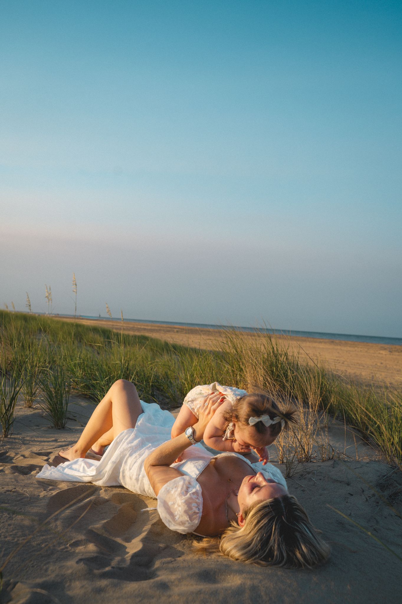 Mother and daughter playing together on sandy beach dunes at golden hour.