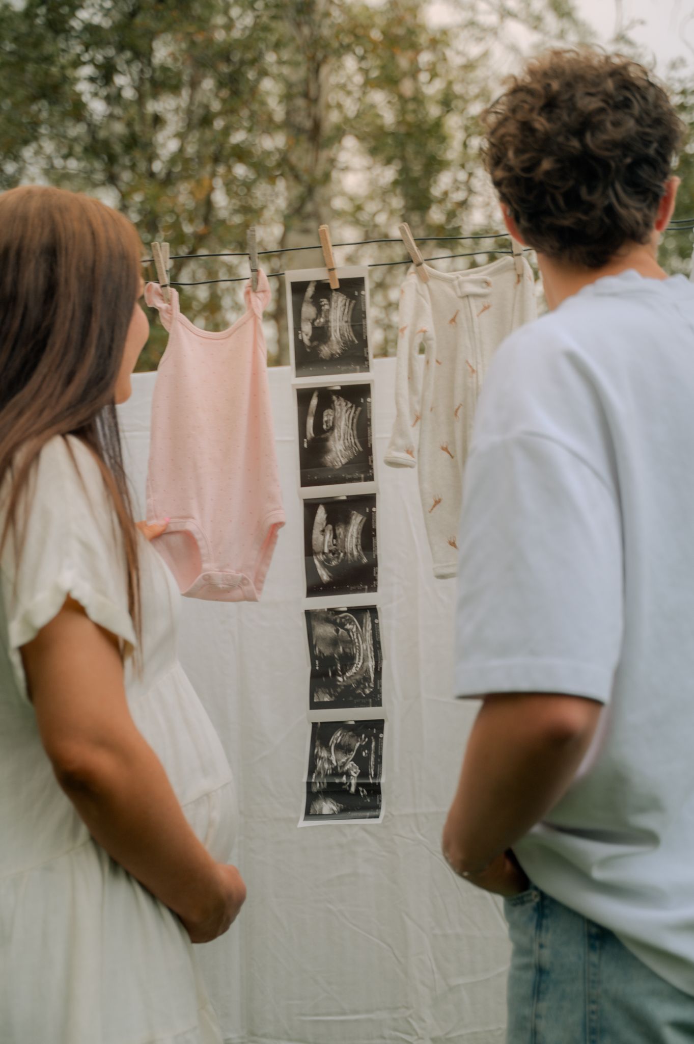 Expectant couple viewing ultrasound photos and baby clothes hanging on a line outdoors.