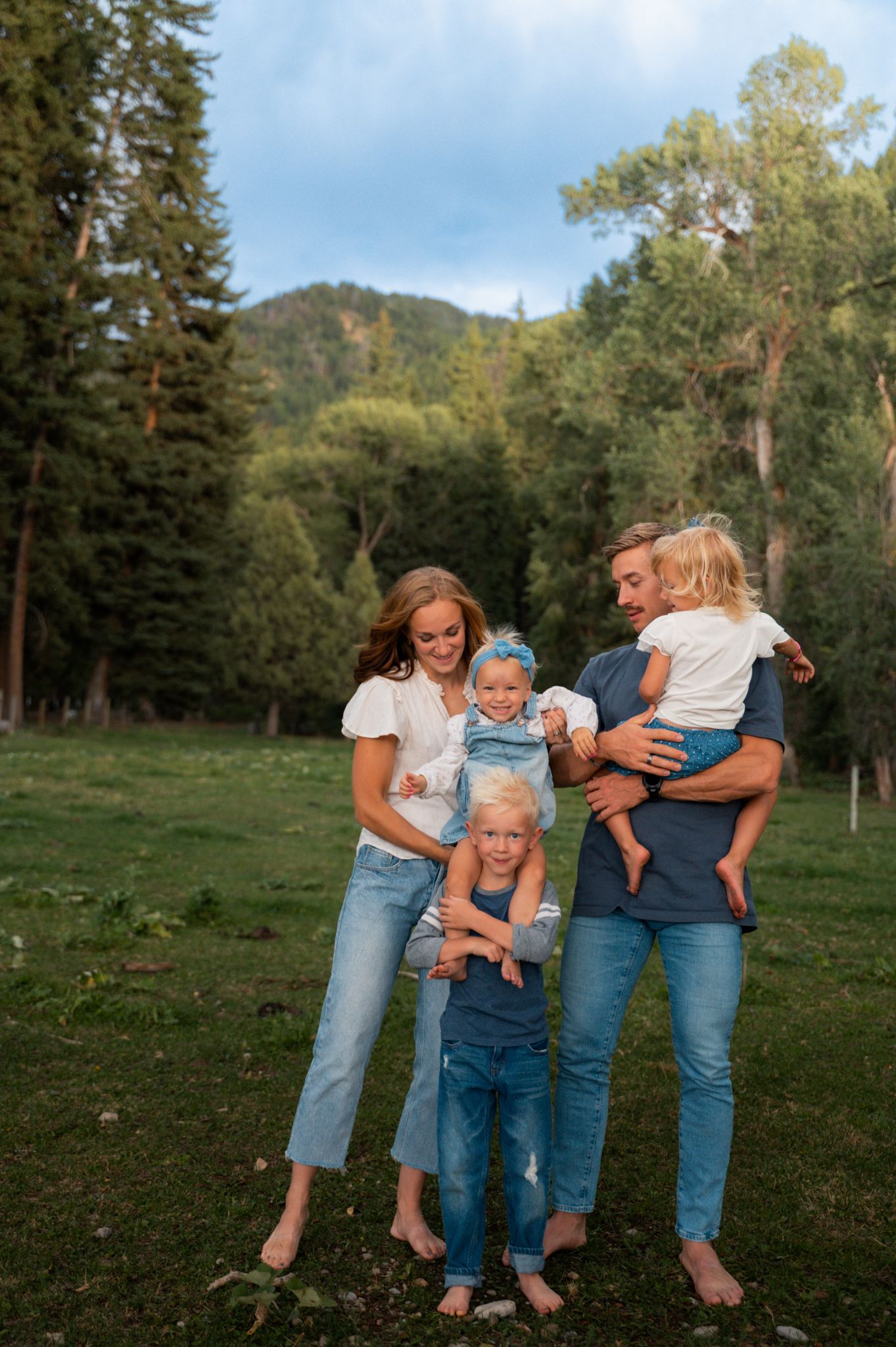 Happy family of five standing together barefoot in a lush green mountain meadow.