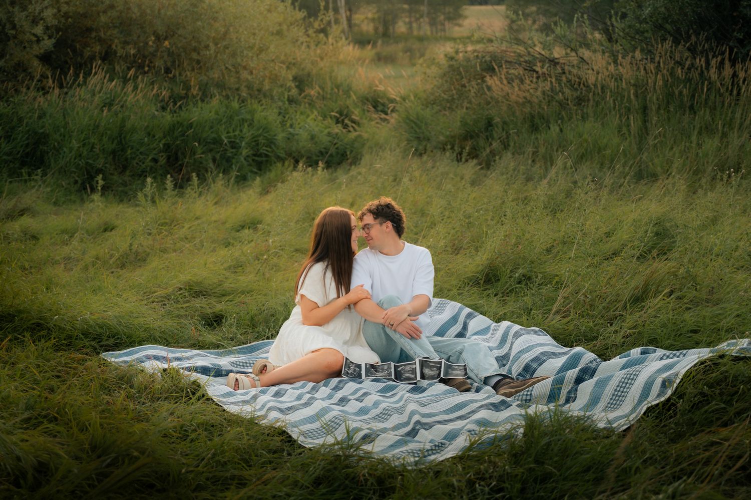 Couple sitting together on a blanket in a lush green meadow, facing each other.