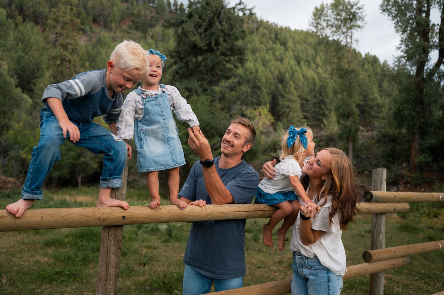 Family of five playing on a wooden fence in a scenic outdoor setting.