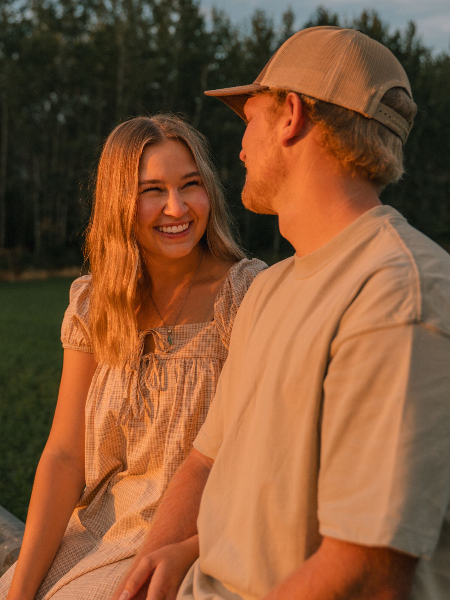 Smiling couple sitting together outdoors laughing during a warm golden hour photo session.