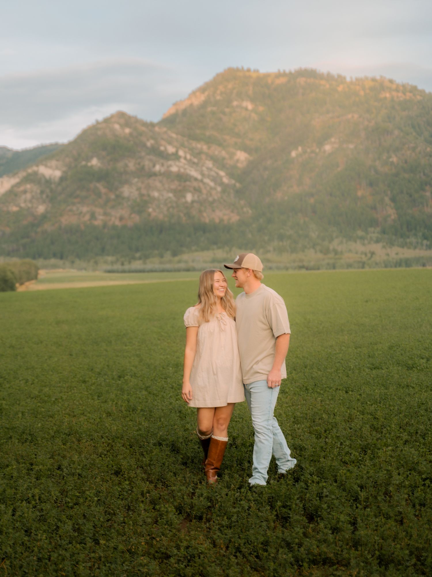 Couple walking through green field with stunning mountain landscape at sunset.