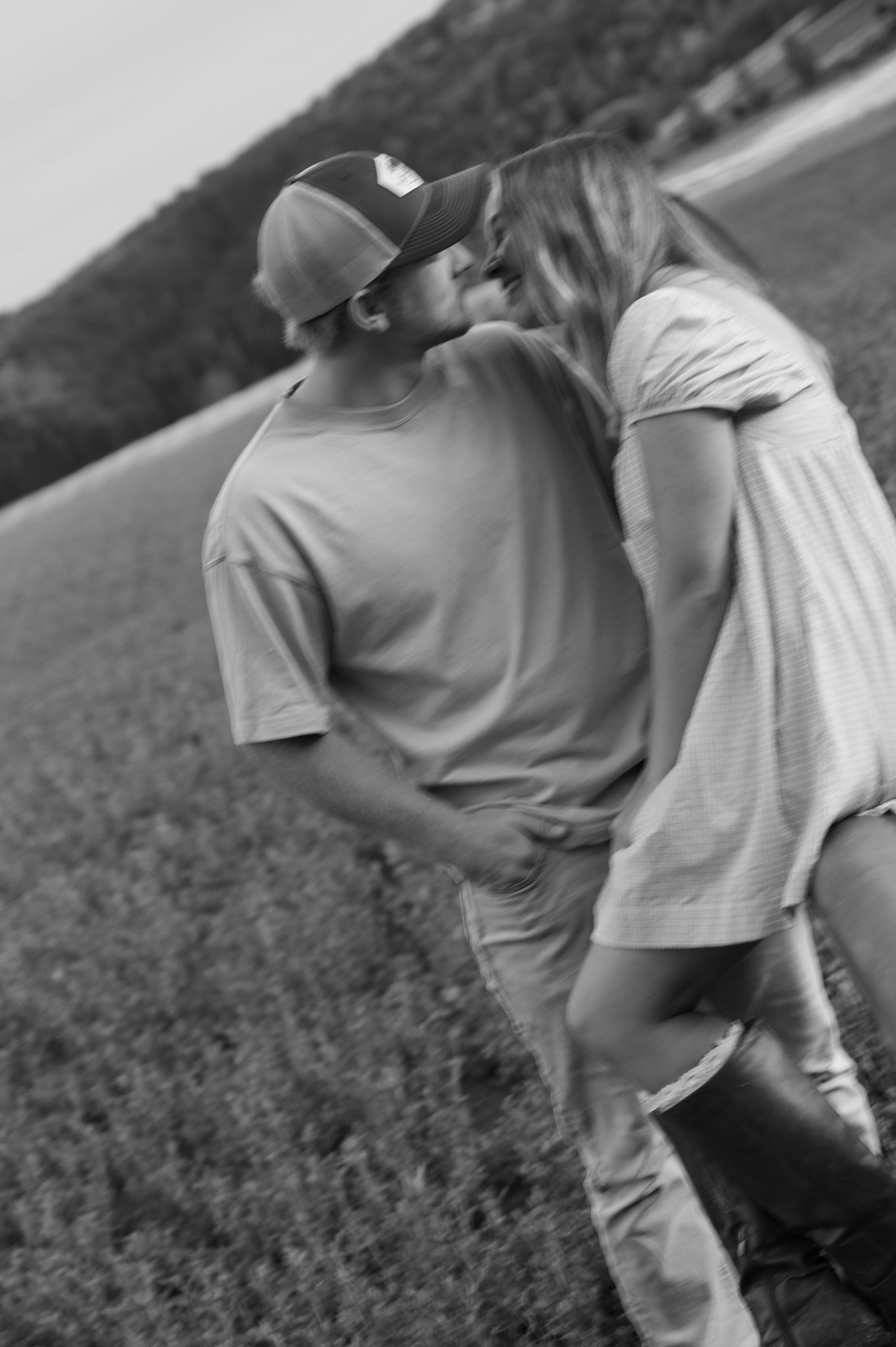 Black and white photo of a couple sharing a kiss in an open field.