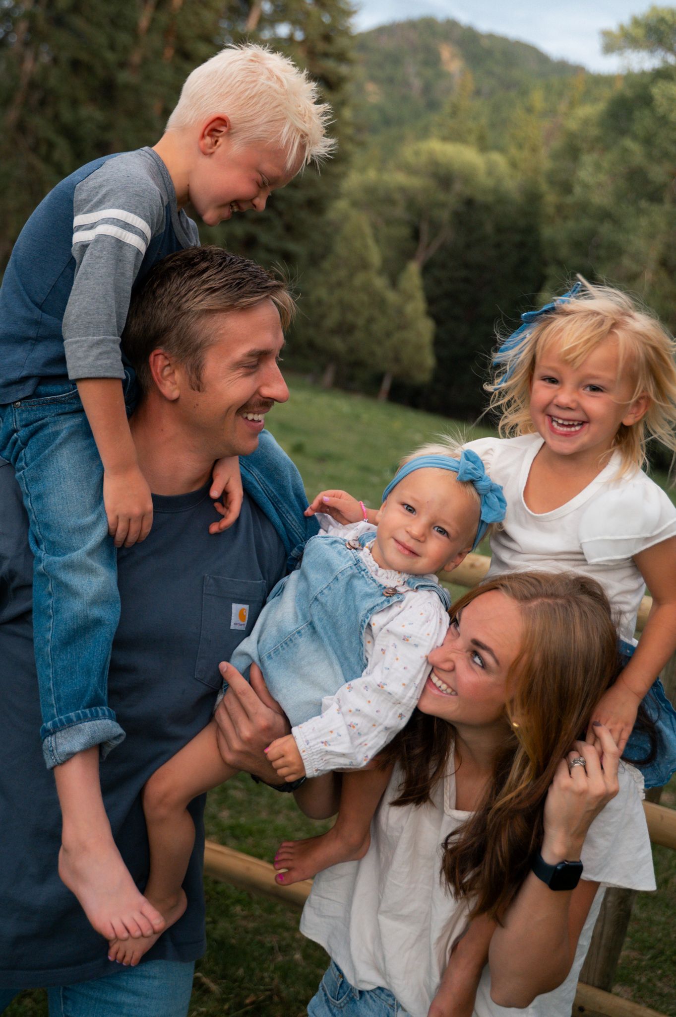 Joyful family of five laughing together outdoors near a wooden fence.