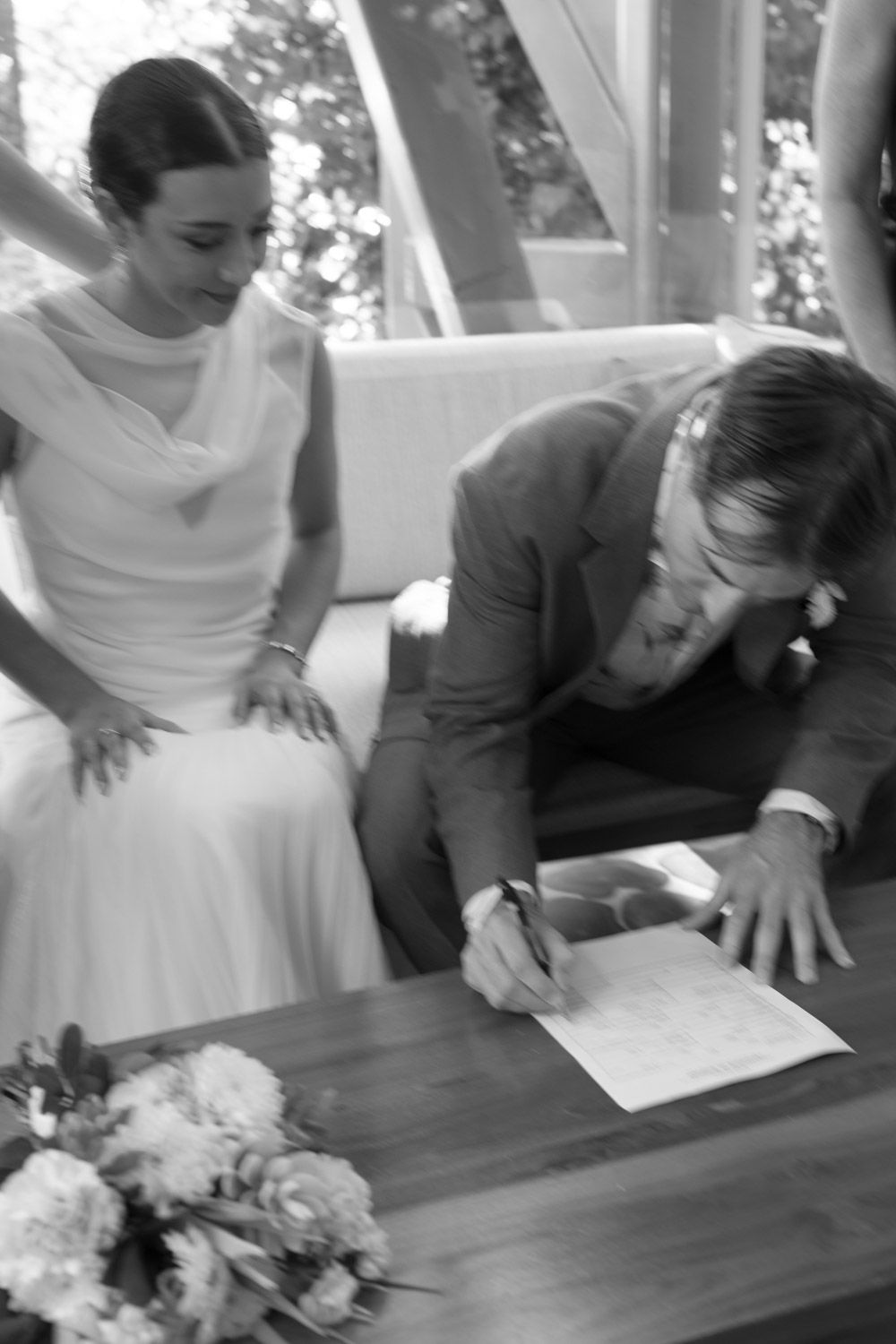 Black-and-white photo of Ryan signing a document beside Sadie on their wedding day in Manuel Antonio, Costa Rica.