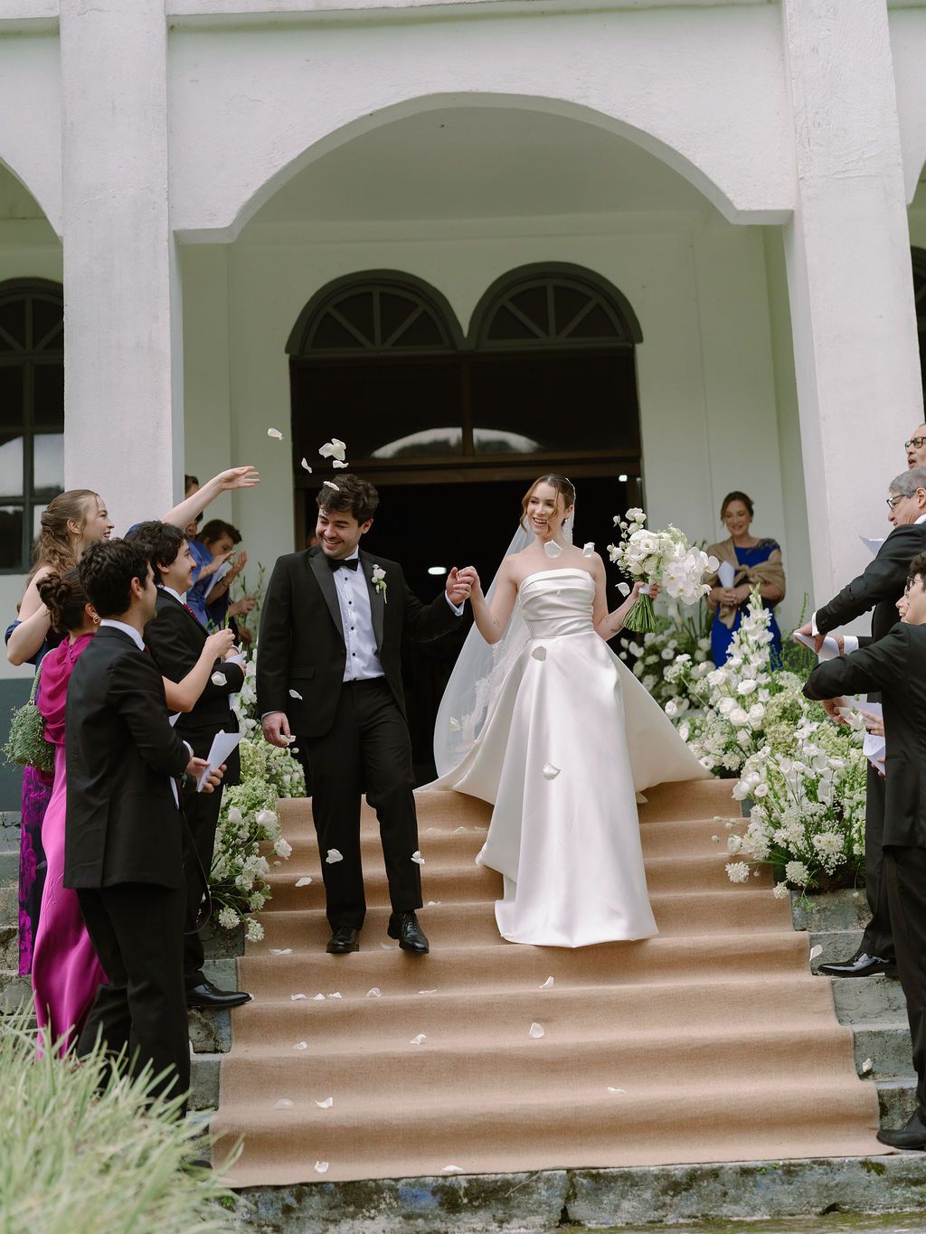 Newlyweds leaving their church ceremony as guests toss flower petals in Monteverde