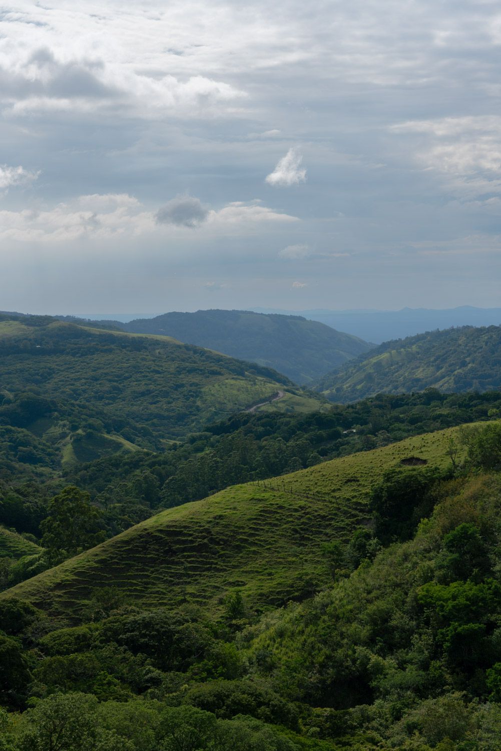 Lush green rolling hills and mountains under a cloudy sky in a scenic tropical landscape in costa rica