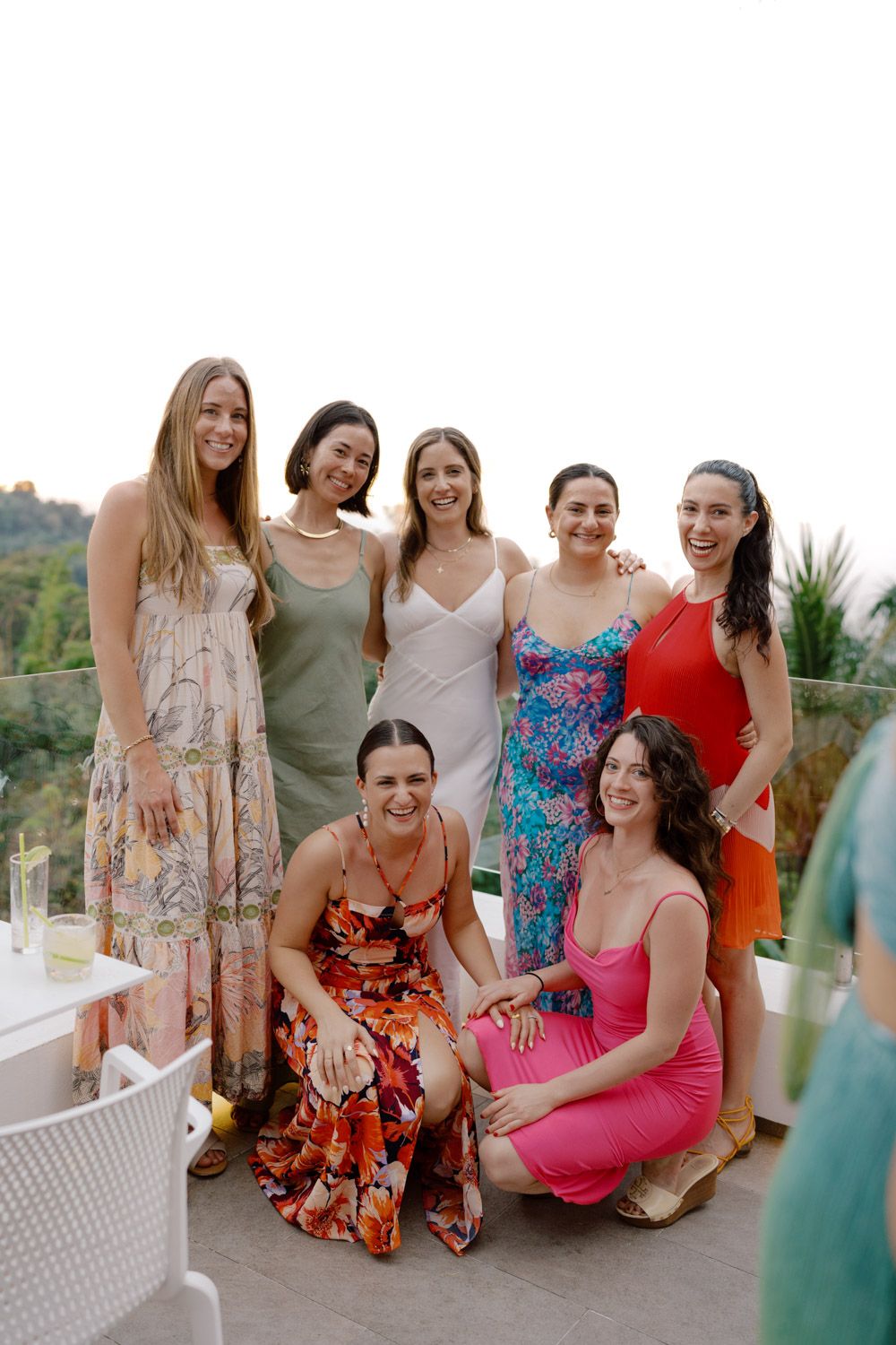 The bride and her friends in colorful summer dresses pose together on a sunny terrace during the welcome party
