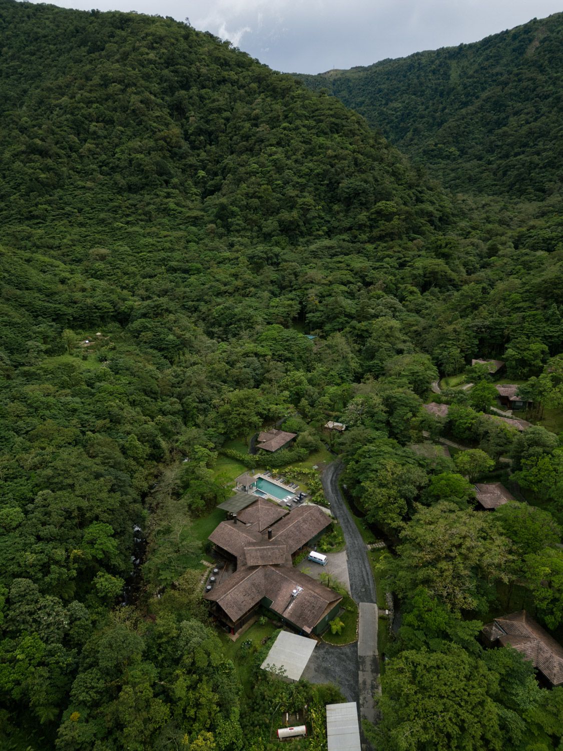 Aerial view of a jungle lodge nestled among lush green tropical forest on a hillside with a visible pool and winding road in costa rica