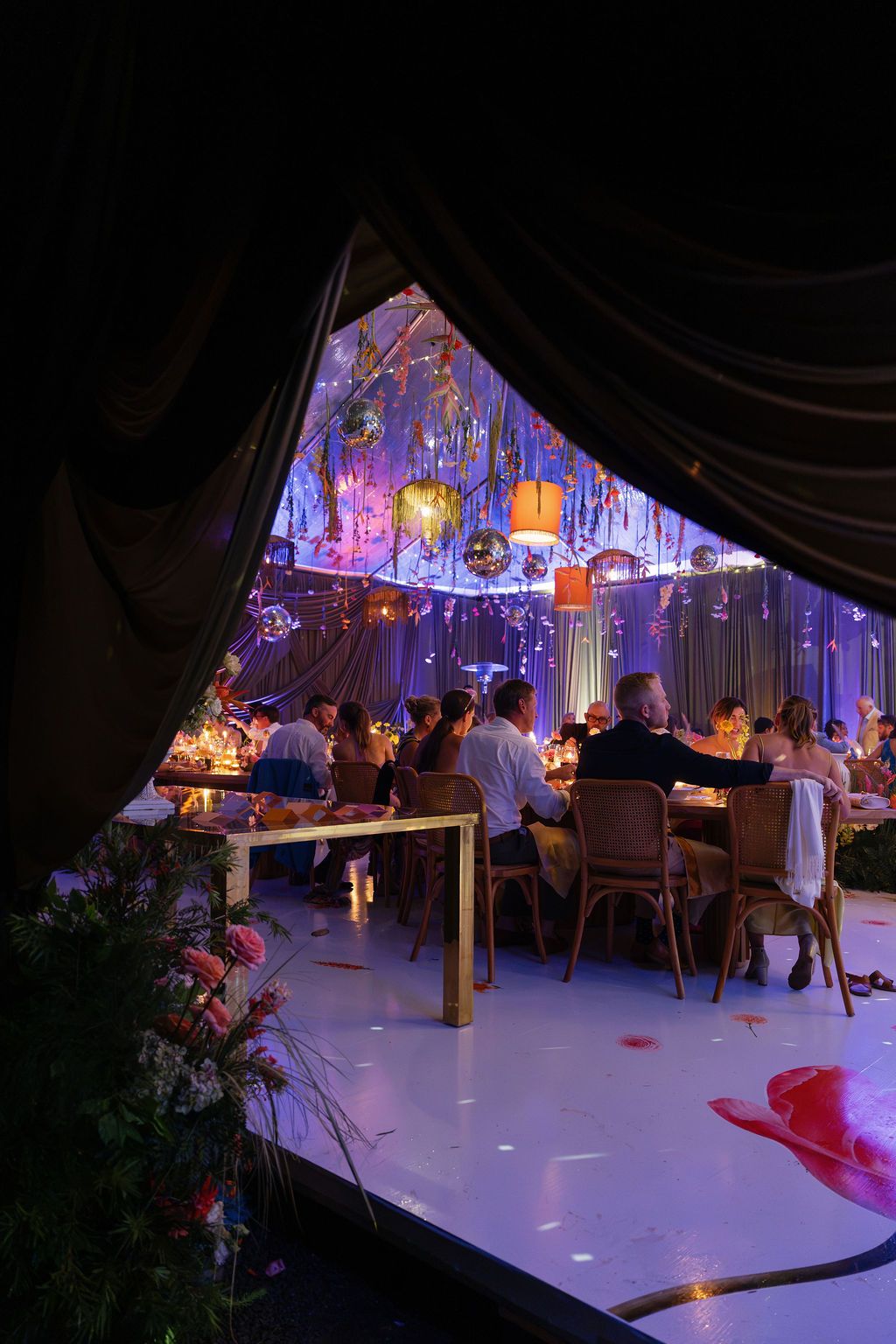 Colorful Costa Rica wedding reception with hanging florals, disco balls, dramatic draping, and candlelit tables