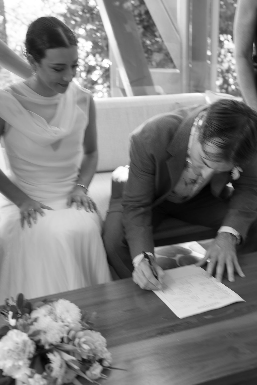 Black-and-white candid photograph of the couple signing wedding documents together.