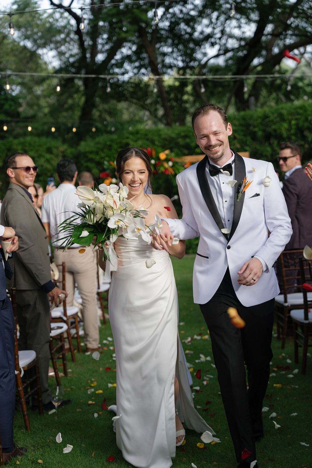 Newlyweds laughing as guests toss petals after their wedding ceremony in Costa Rica.
