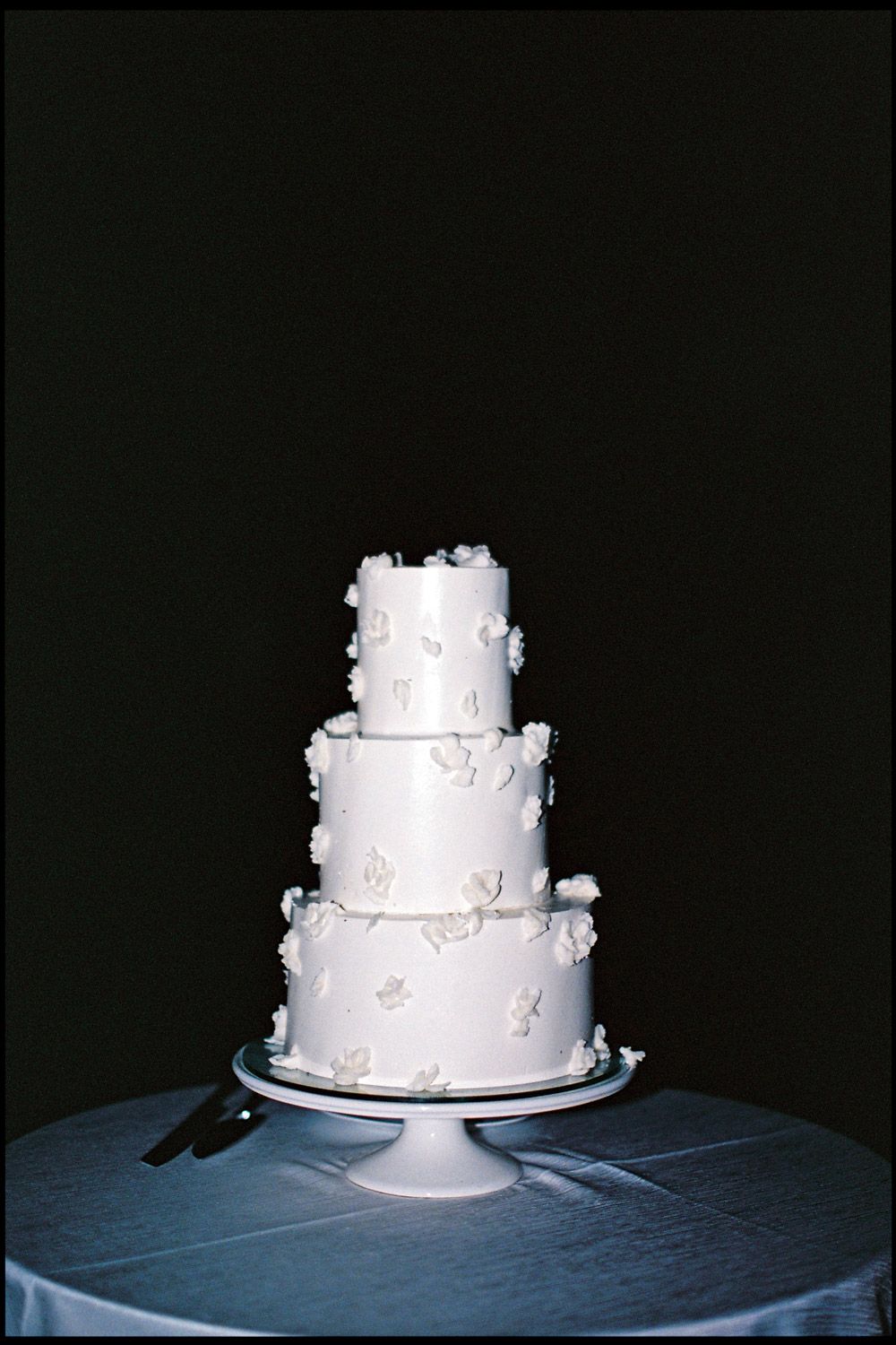 Three-tier white wedding cake with delicate floral decorations on a blue tablecloth in Costa Rica.