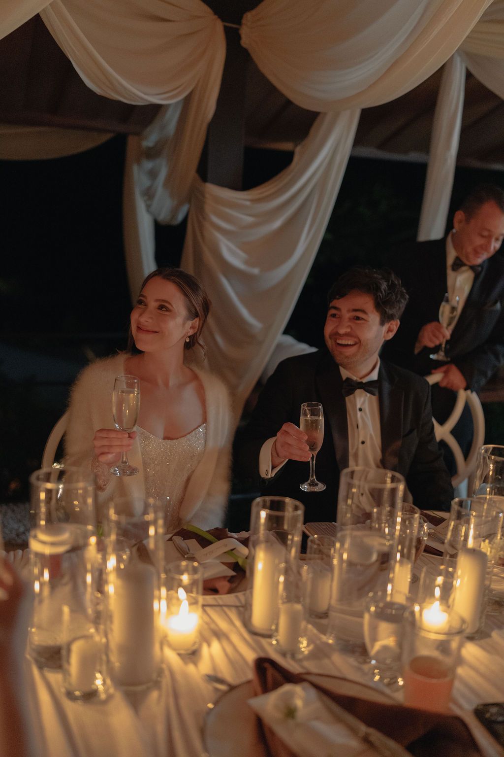 Bride and groom raising champagne glasses during their candlelit Monteverde wedding reception