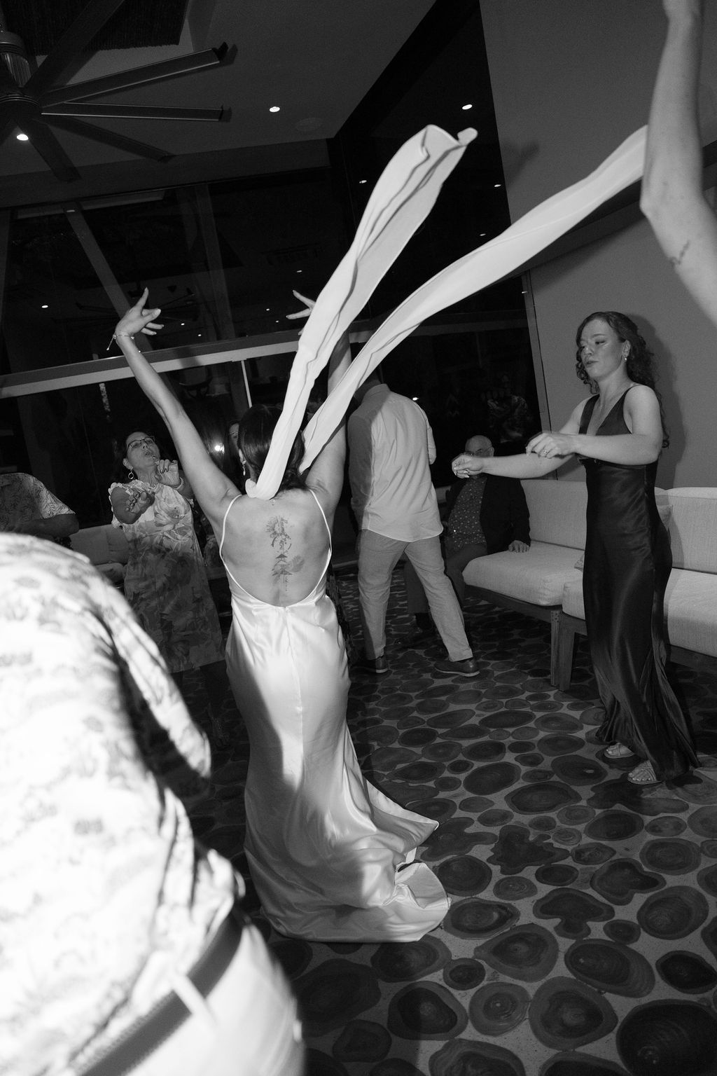 Black-and-white candid image of the bride dancing with guests during the wedding party.