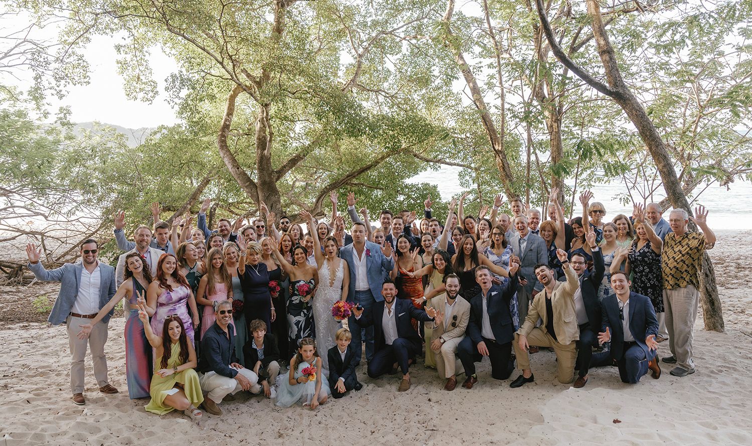 Bride and groom surrounded by cheering wedding guests beneath beachside trees in Costa Rica