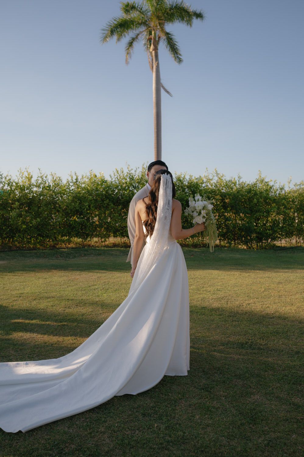 Bride with a flowing veil and bouquet beneath a palm tree at Hacienda Pinilla, Costa Rica.