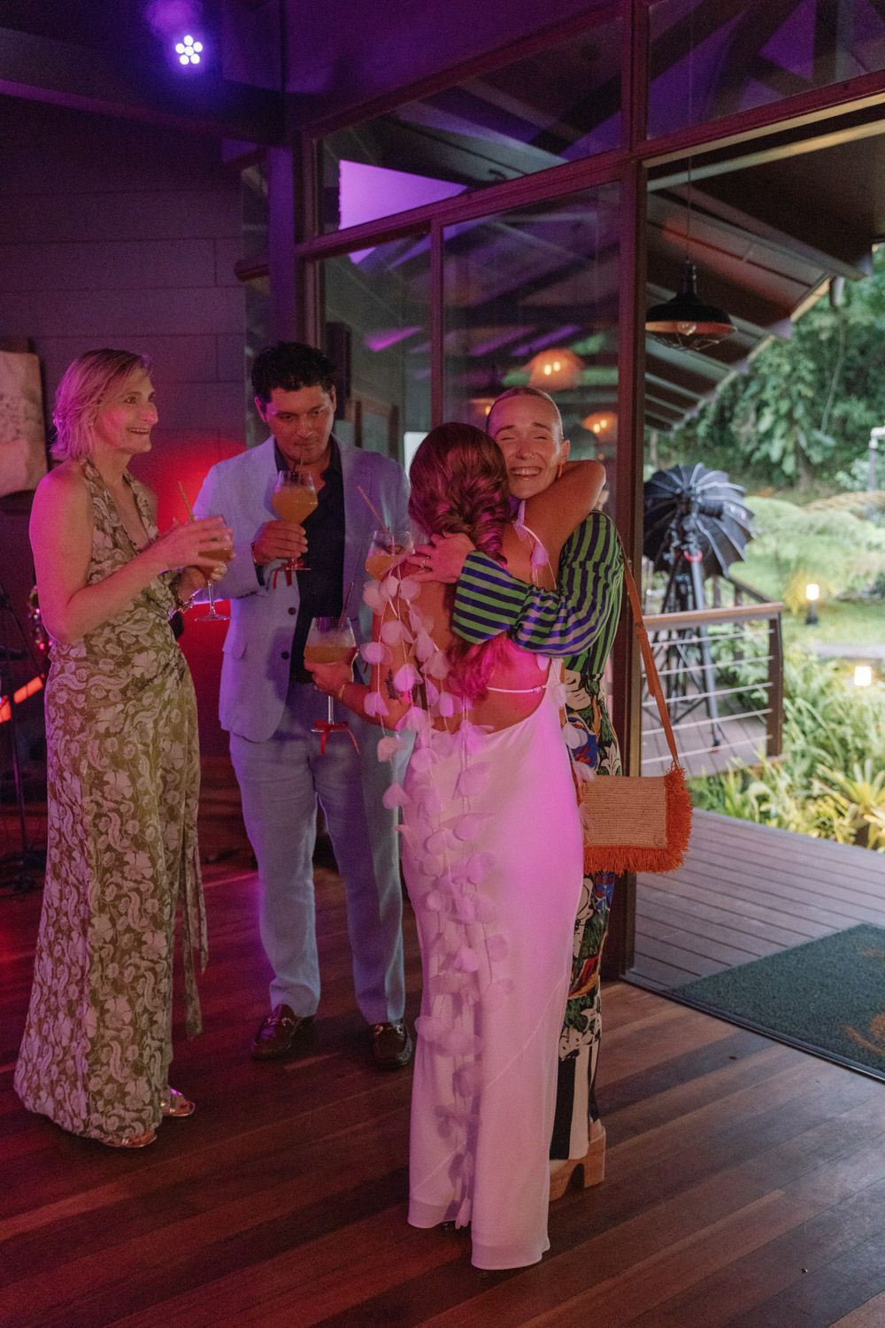 Guests sharing a hug and drinks during a wedding welcome party on a wooden terrace in Costa Rica.