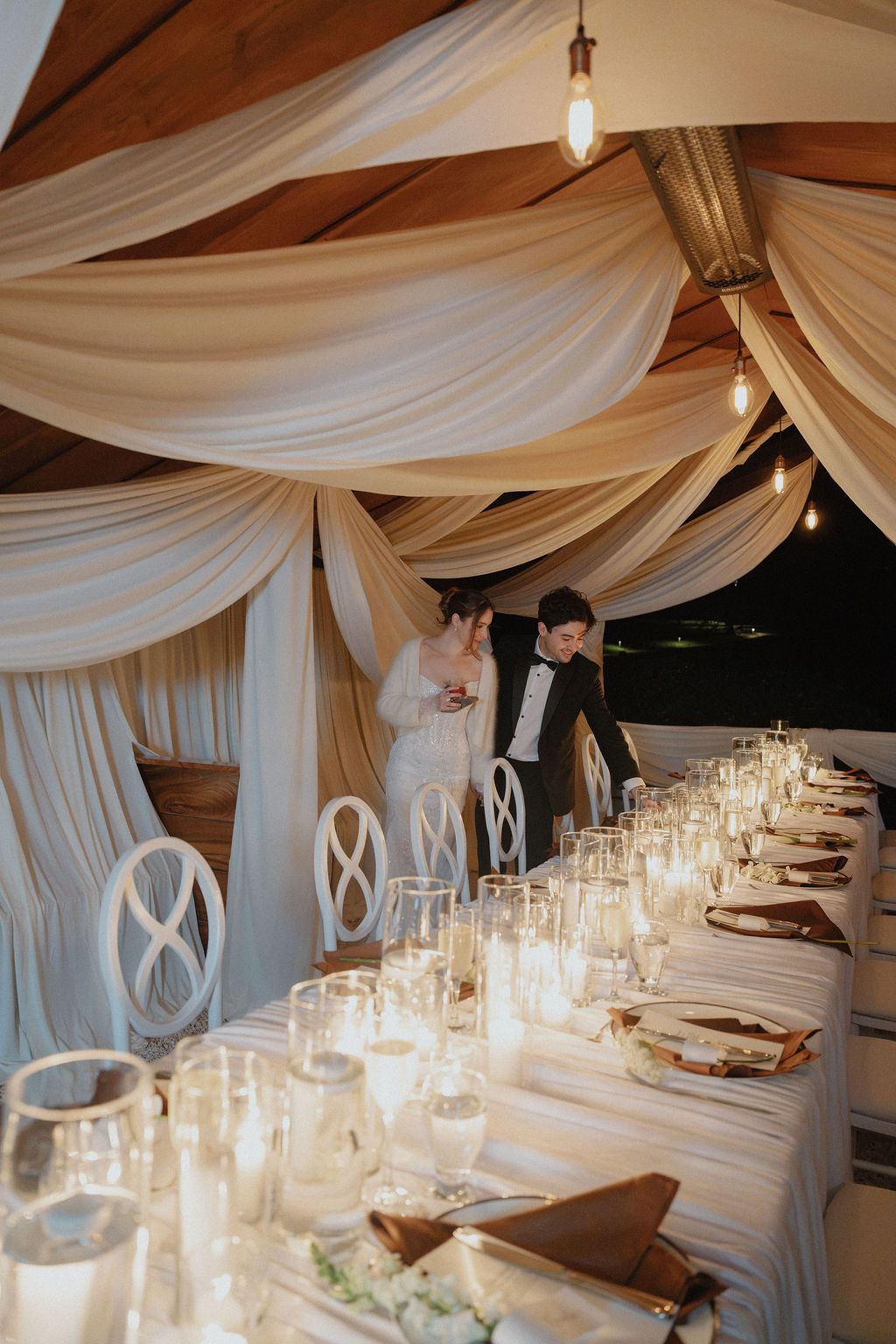 Bride and groom arriving at their candlelit wedding dinner beneath white drapery