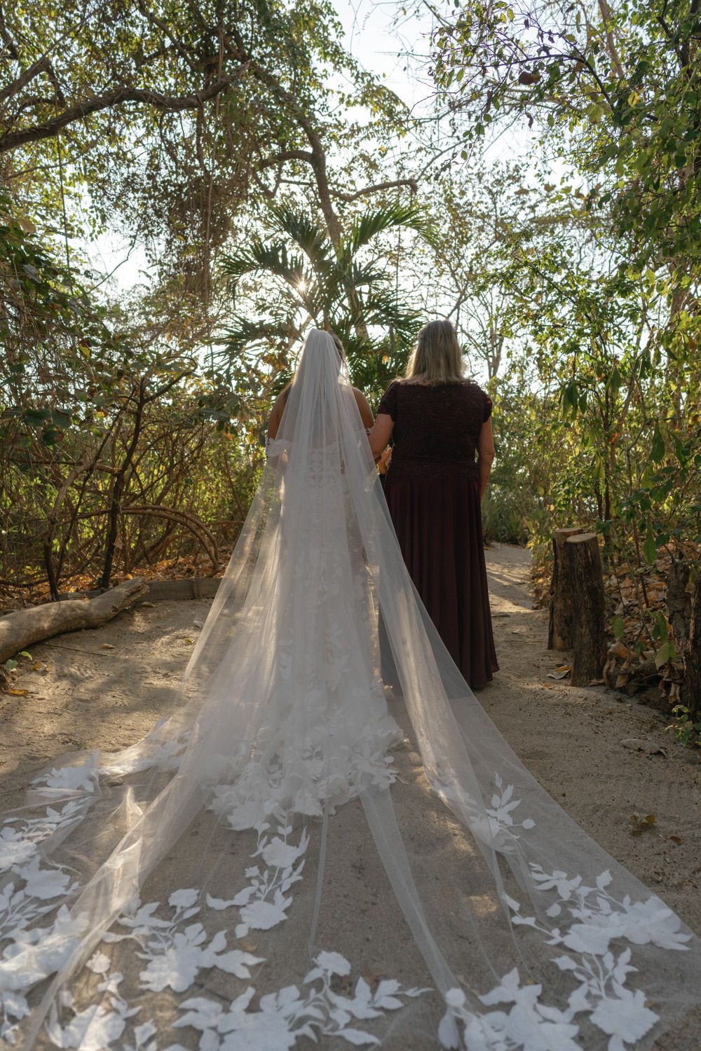 Bride and her mother walk a sandy path through tropical trees in Tamarindo
