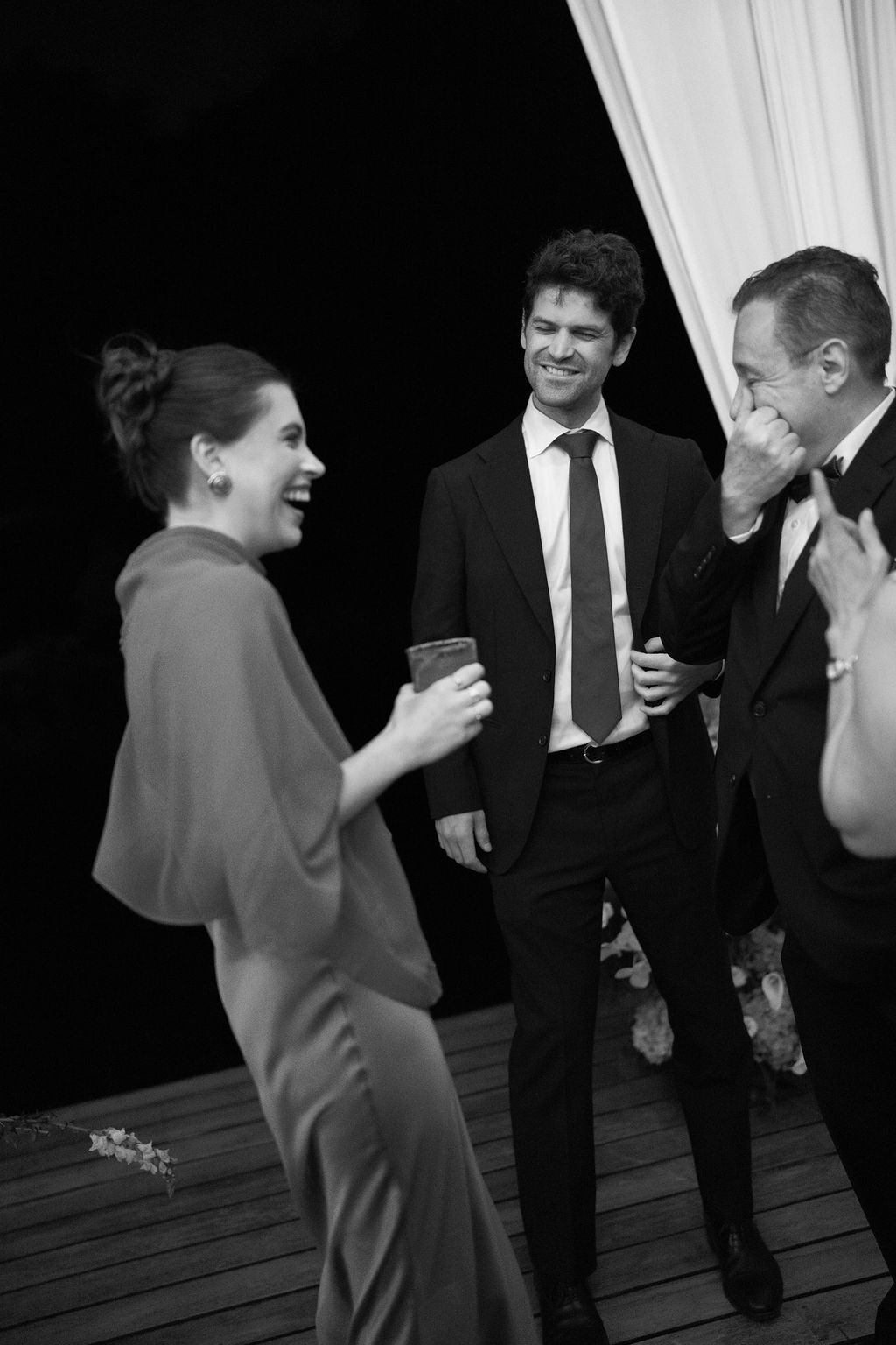 Candid black and white photograph of wedding guests laughing together during the reception