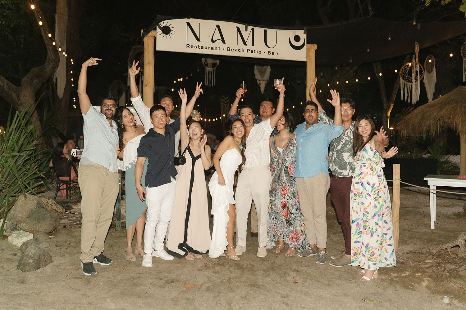 Group of friends posing and celebrating outside Namu Restaurant on a beach at night.
