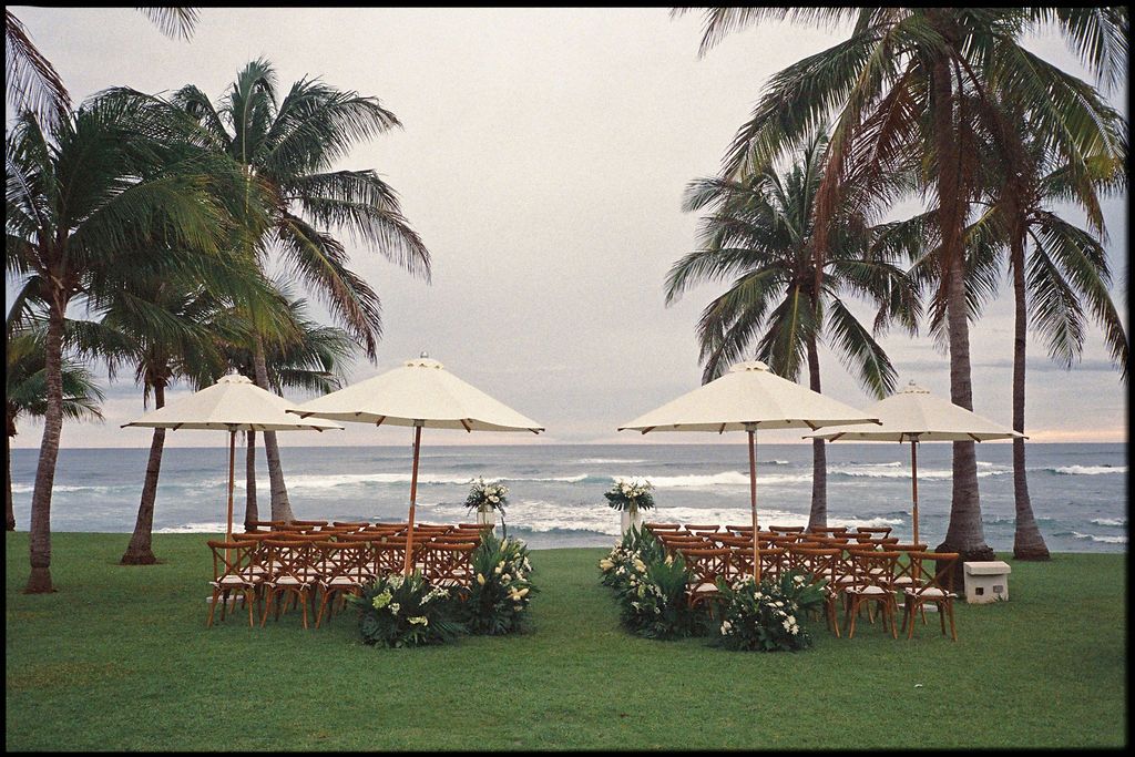 Oceanfront wedding ceremony setup with wooden chairs and white umbrellas in Costa Rica.