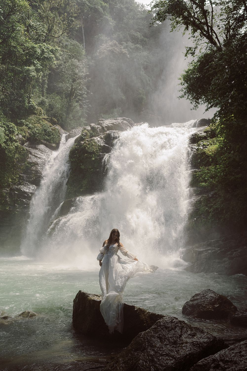 Bride standing in front of a tropical waterfall during an adventurous elopement in Costa Rica.