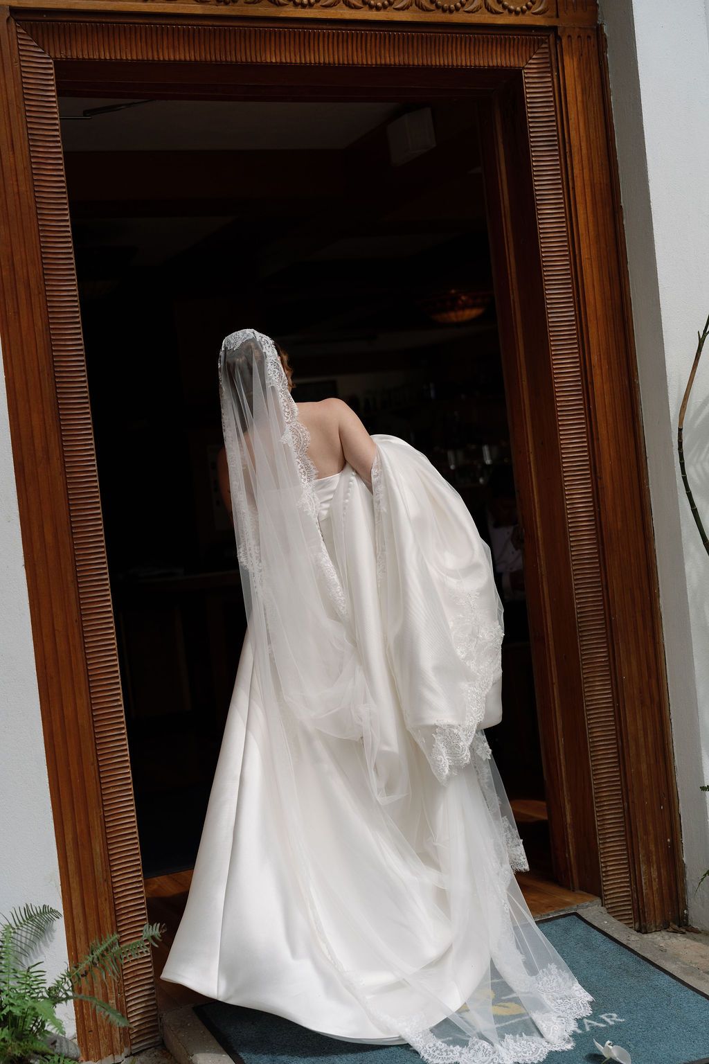 Bride walking through a doorway with her long lace wedding veil trailing behind her