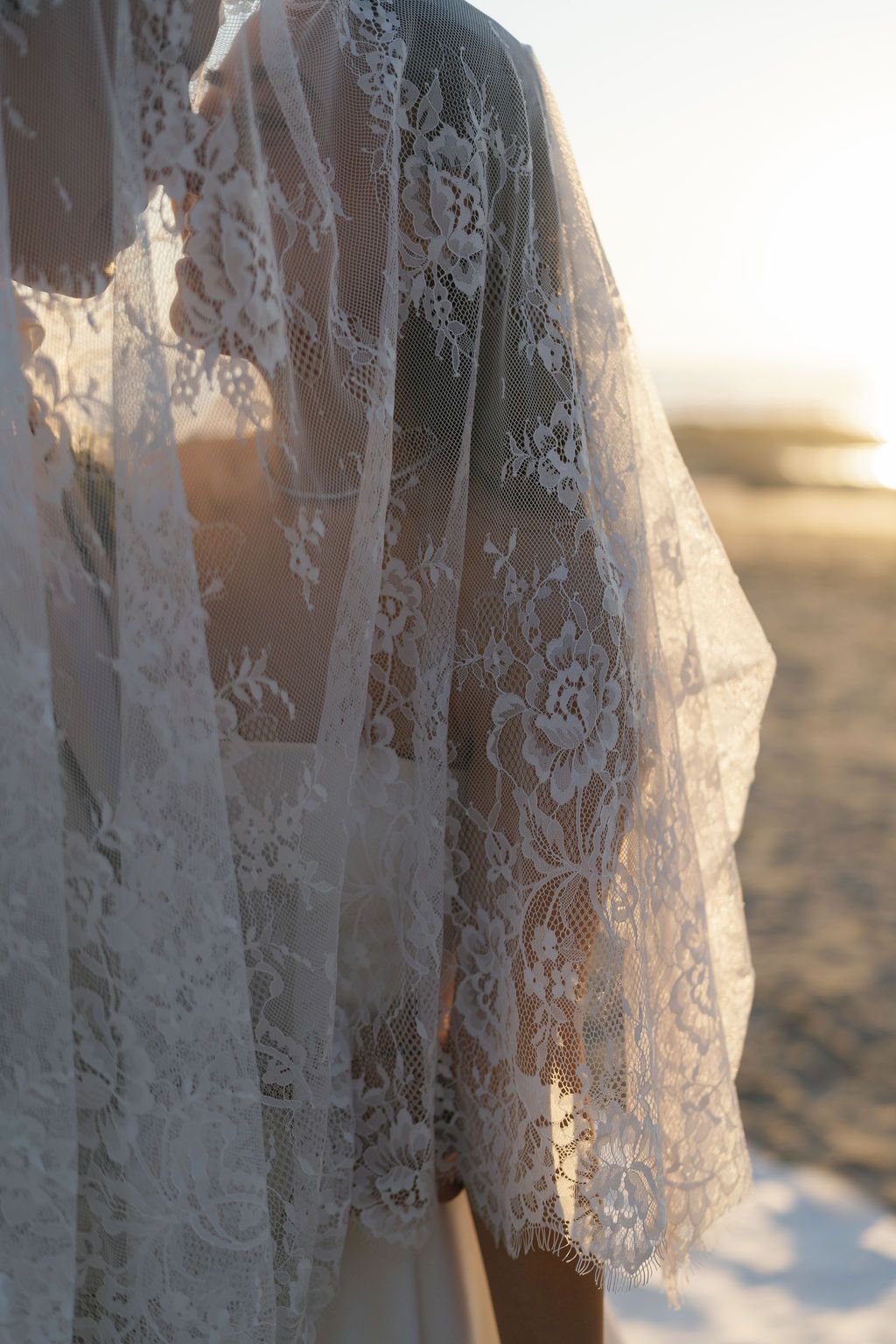 Close-up of a bride's lace veil glowing in the evening light by the beach.